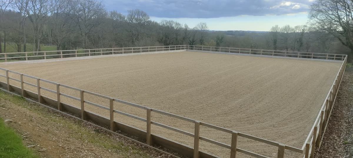 A completed riding arena seen along its length, surface freshly levelled