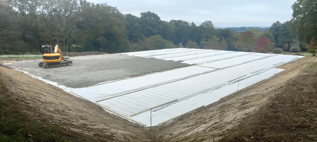 Geotextile membrane being rolled out over a compacted stone arena base